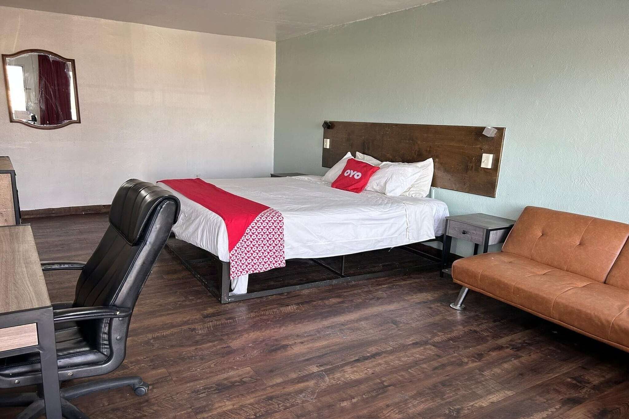 A hotel room with a bed, a desk, a chair, a sofa, and a mirror.