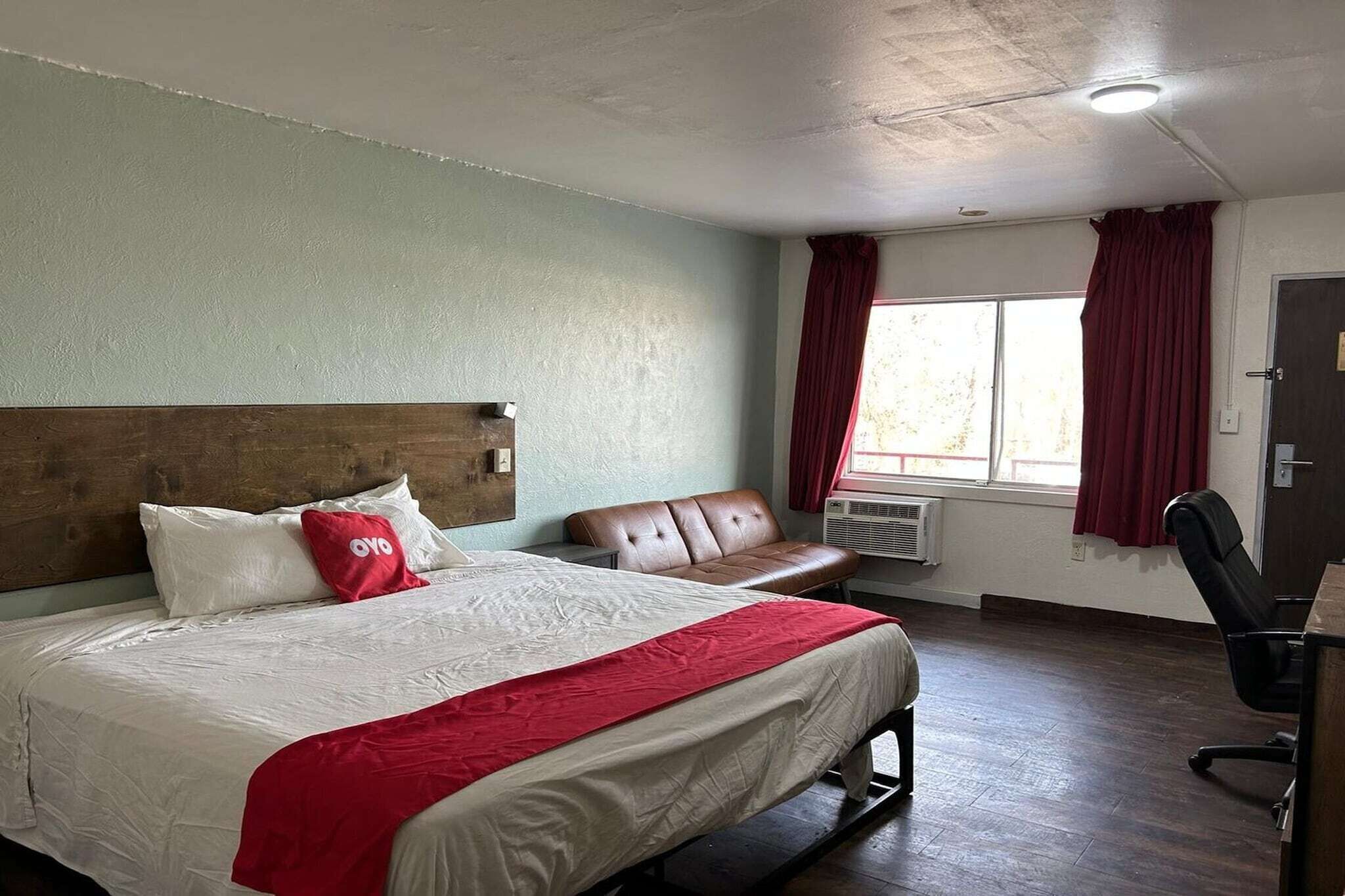 Une chambre d’hôtel avec un lit, un canapé en cuir, un bureau et une fenêtre avec des rideaux.