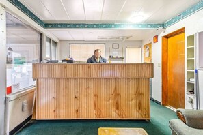 Un mostrador de recepción con detalles de madera, suelo cubierto de alfombra verde y una ventana con persianas visibles.
