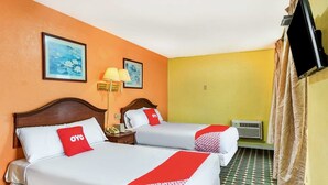 Two beds with white bedding and red accents, a lamp, a TV, and a patterned carpet.