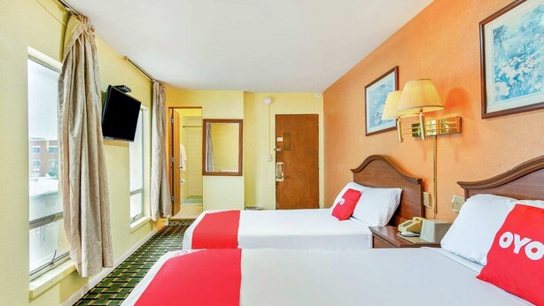 A hotel room with two beds, a TV, a lamp, and a door leading to a balcony.