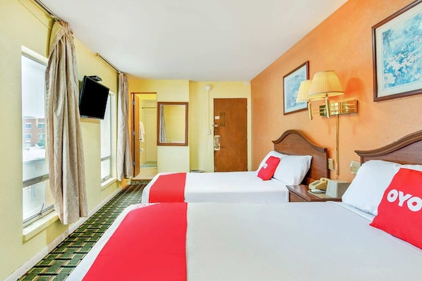 A hotel room with two beds, a TV, a lamp, and a door leading to a balcony.