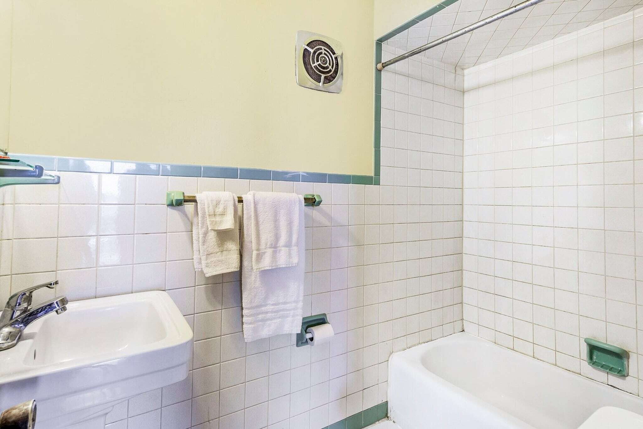 Un baño con lavamanos, dos toallas, un ventilador y una bañera.