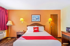A hotel room with a bed, two bedside lamps, a nightstand with a phone, a wooden door, and a framed picture on the wall.