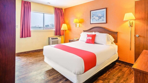 Una habitación de hotel con una cama grande, dos lámparas de noche, una ventana con cortinas, un equipo de aire acondicionado y una puerta de madera.