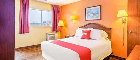 A hotel room with a large bed, two bedside lamps, a window with curtains, an air conditioning unit, and a wooden door.