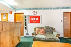 A reception area with a wooden desk, a green sofa, a clock, and a sign that reads 'OYO HOTEL.'