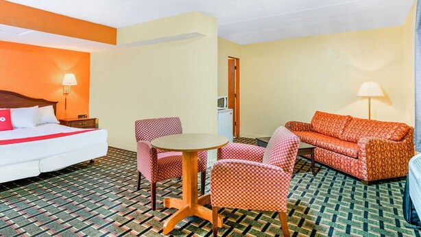 Une chambre d’hôtel comprenant un lit, un canapé, deux fauteuils, une petite table et une lampe.