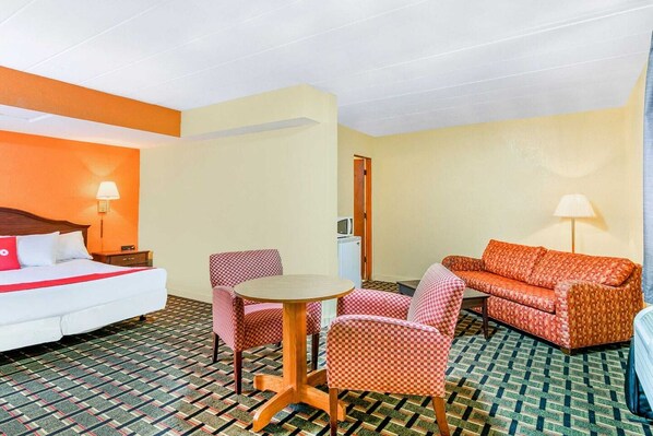 A hotel room with a bed, a sofa, two armchairs, a small table, and a lamp.