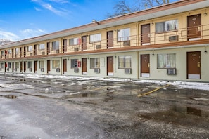 Fila de habitaciones de motel con puertas individuales, estacionamiento y cielo despejado.