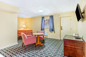 A room with a patterned floor, a sofa set, a table, a TV mounted on the wall, and a wooden cabinet.