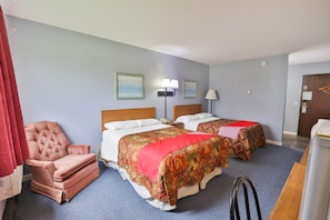 A hotel room with two beds, a chair, a desk, and a door.