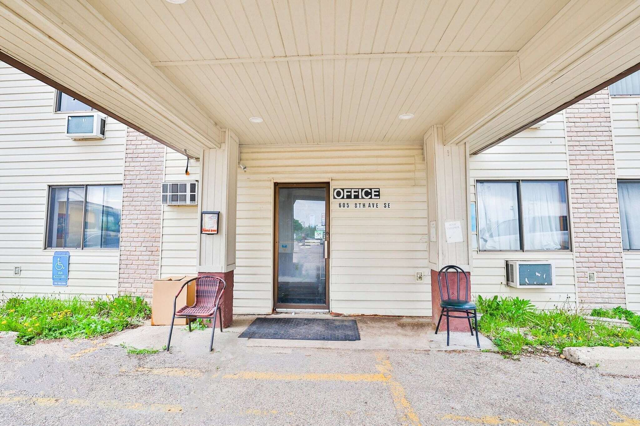 Un edificio con un acceso cubierto, un cartel que dice 'OFFICE 605 8TH AVE SE' y dos sillas afuera.