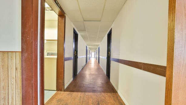 Un long couloir étroit, doté d’un plancher en bois et de murs blancs rehaussés de moulures sombres.