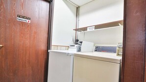 Une pièce privée avec une porte en bois, un lave-linge blanc et une étagère sur laquelle se trouve une machine à café.