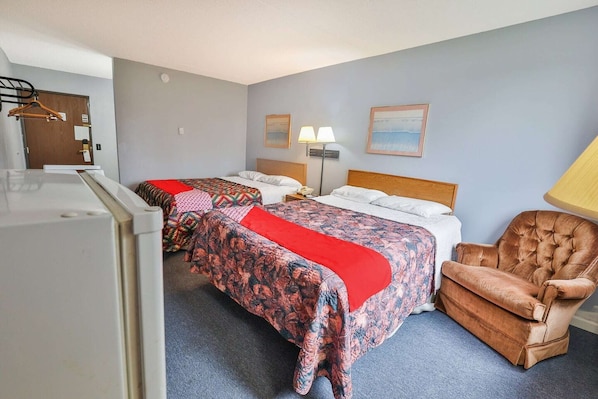 A hotel room with two beds, a chair, a desk, and a lamp.