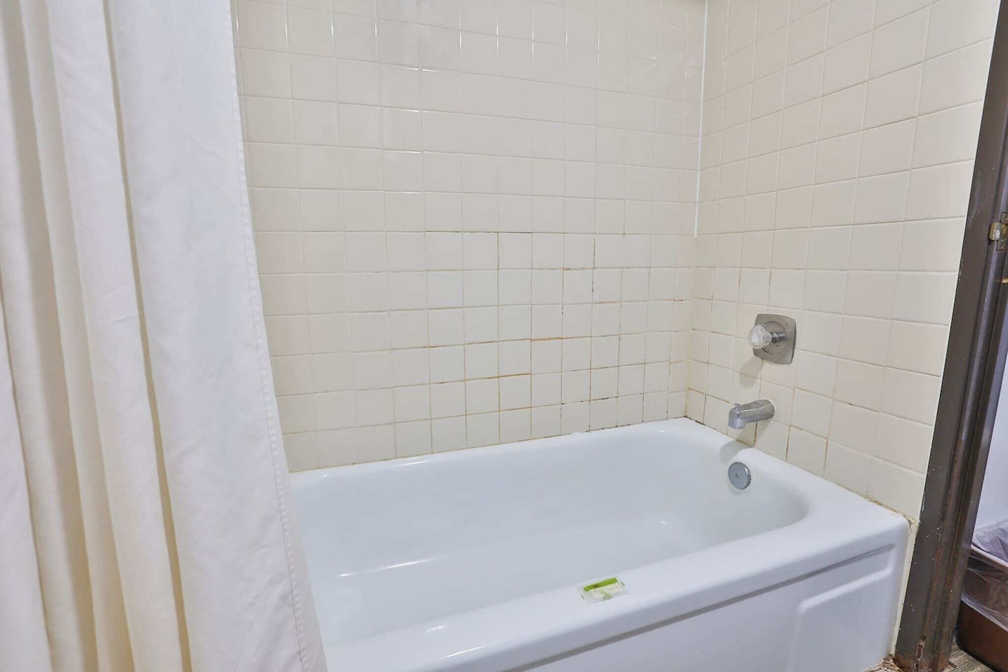 Une salle de bain avec une baignoire blanche, des murs recouverts de carreaux blancs et un rideau de douche.