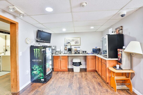 A compact kitchen with a refrigerator, microwave, coffee maker, and a TV mounted on the wall.