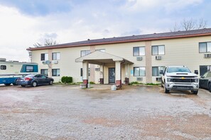 A two-story motel with a covered entrance, a gravel driveway, and a parked car and truck. - Pipestone|Queen Bed|Nsmk (Pipestone)