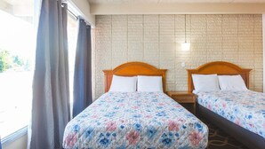 Hotellihuone, jossa on kaksi sänkyä, tiilikuviolla koristeltu seinä ja ikkuna, jossa on verhot.