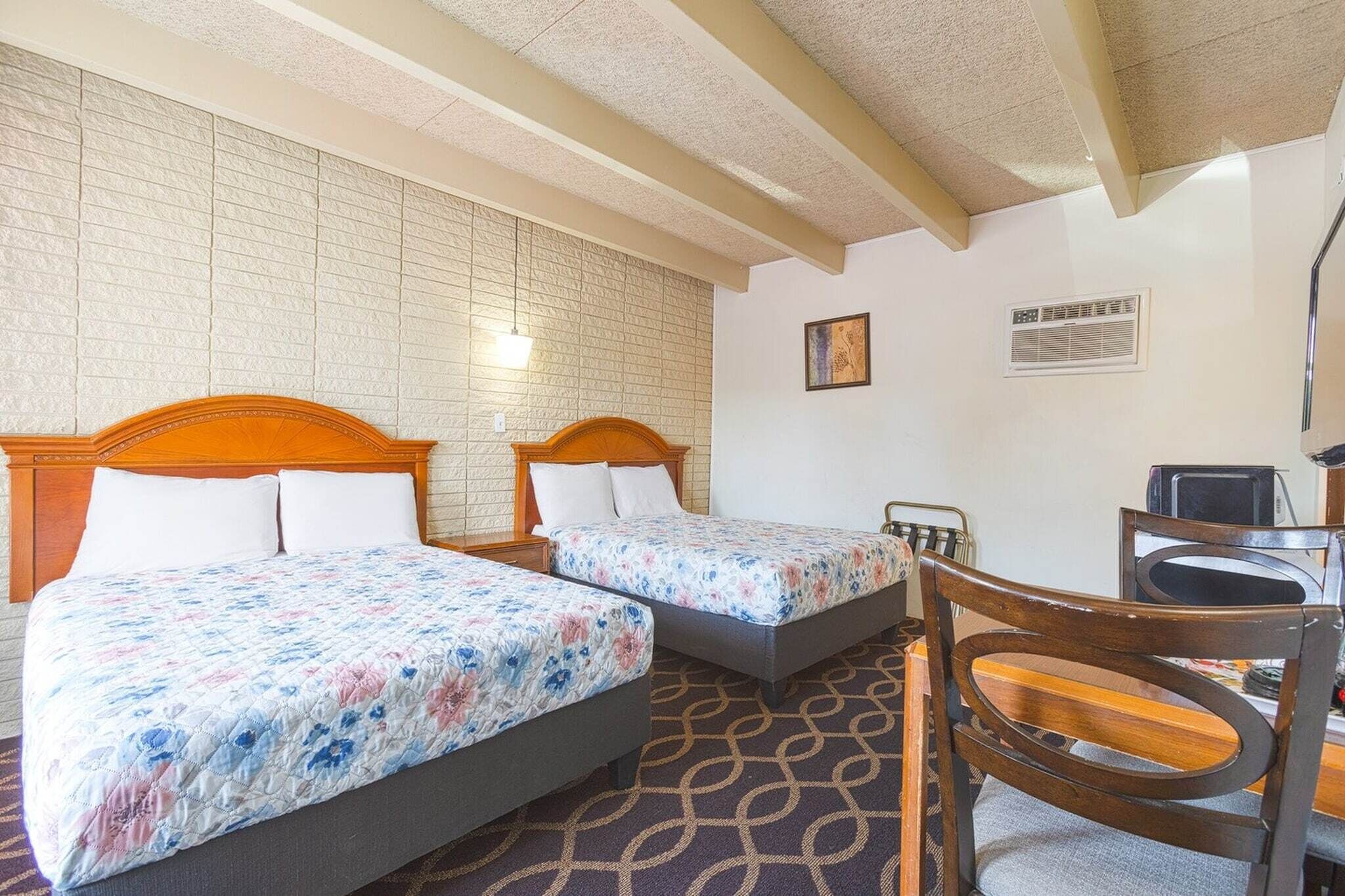 Une chambre d’hôtel avec deux lits, un bureau, une chaise et une moquette à motifs.