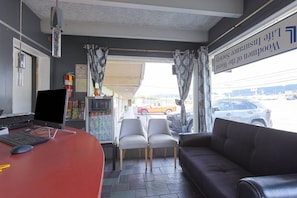 Una habitación con escritorio, dos sillas, sofá, computadora y vista a la calle.