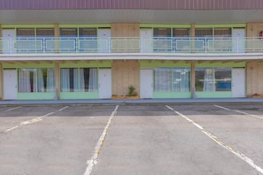 Un motel de dos pisos con habitaciones numeradas, un estacionamiento y un pequeño jardín.