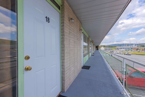 A corridor with a white door marked '18', a brick wall, and a covered walkway overlooking a road with vehicles.
