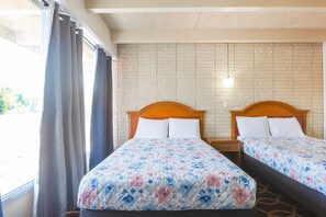 A hotel room with two beds, a brick-patterned wall, and a window with curtains.
