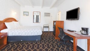 A hotel room with a bed, desk, chair, TV, and a coffee maker.