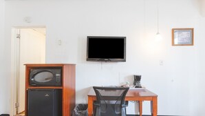 A hotel room with a flat-screen TV, a microwave, a refrigerator, a desk with a chair, and a coffee maker.
