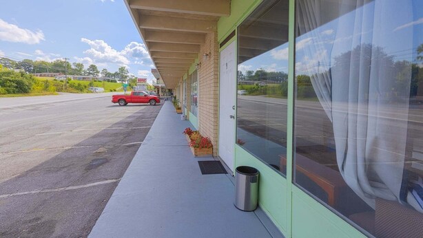 A building with a covered outdoor area, a parked red car, and a clear sky.