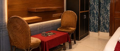 A hotel room with a wooden wall, a TV mounted above a table with two chairs, a wardrobe, and a bed with a red blanket.