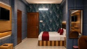 A hotel room with a bed, a TV, a wooden wardrobe, a mirror, and a small table. - Jannat Hotel - Solan (Solan)
