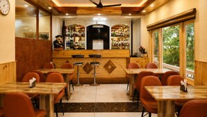 A restaurant with wooden tables and chairs, a bar area with bottles, and a large window with a view. - Jannat Hotel - Solan (Solan)