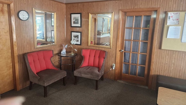 A room with wooden paneled walls, two red upholstered chairs, a small round table with a lamp, and a door with a frosted glass panel. - King Bed|Non-Smoking (Quinter)