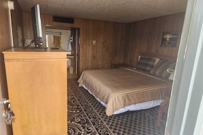 A bedroom with a bed, a wooden desk, a computer, and a patterned rug.