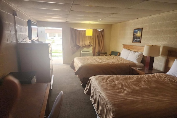 A hotel room with two beds, a desk, a chair, a lamp, and a painting on the wall.