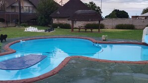 Piscina com borda de pedra, um tabuleiro de xadrez e um cão por perto.