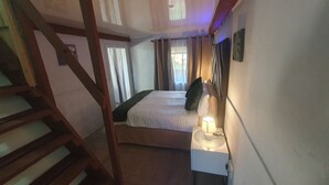 Um quarto com cama, mesa de cabeceira com abajur, janela com cortinas e escada.