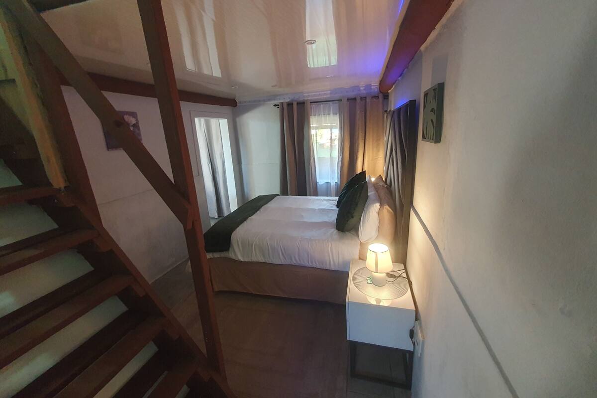 Une chambre à coucher avec un lit, une table de chevet avec une lampe, une fenêtre avec des rideaux et un escalier.