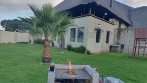 Um quintal com churrasqueira, uma palmeira e uma casa com telhado de palha.