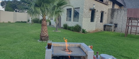 A backyard with a barbecue grill, a palm tree, and a house with a thatched roof.