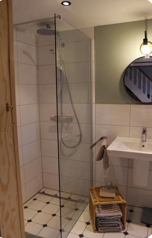 Ein Badezimmer mit einer Duschkabine, einem Waschbecken mit Spiegel und einem Handtuchhalter mit Handtüchern.