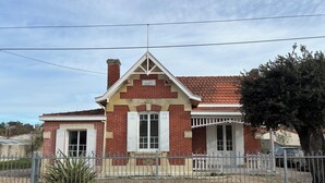 A two-story brick house with a red-tiled roof, white shutters, and a small porch. - A home in Soulac, just a stone's throw from downtown and the beach (Soulac-sur-Mer)