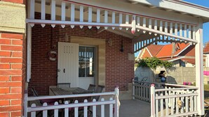 A brick house with a white porch, a door, and a small outdoor seating area. - A home in Soulac, just a stone's throw from downtown and the beach (Soulac-sur-Mer)