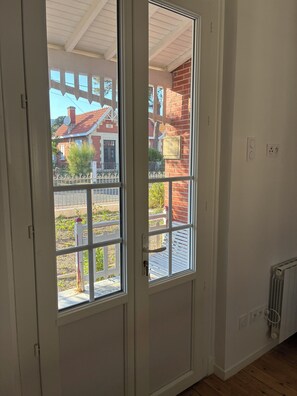 Ein Zimmer mit einer weißen Tür, einem Fenster mit Blick auf ein Backsteingebäude und einem Heizkörper an der Wand.