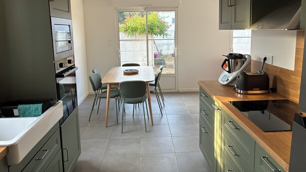 A modern kitchen with a dining table, chairs, and a view through a large window. - A home in Soulac, just a stone's throw from downtown and the beach (Soulac-sur-Mer)