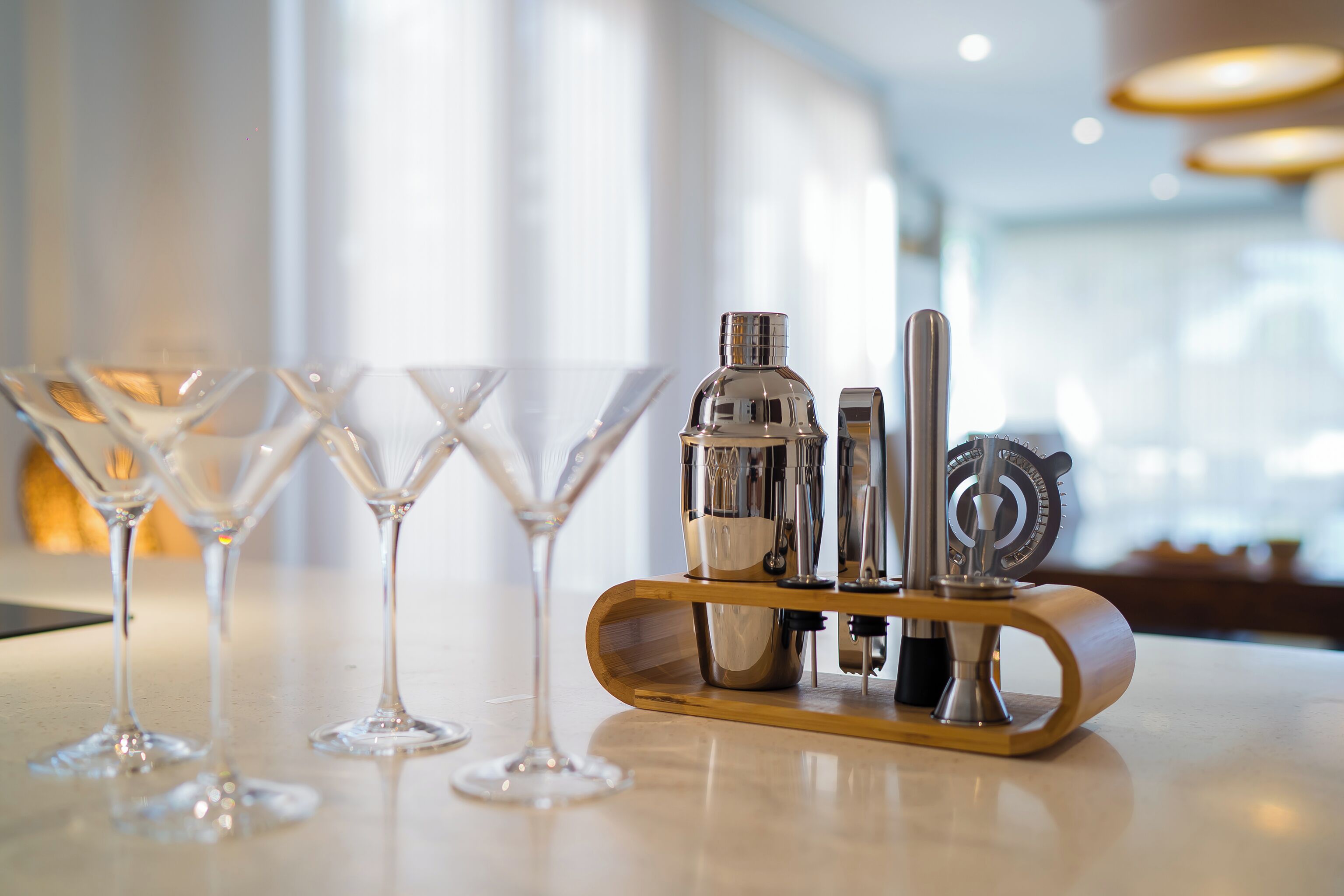 Un espace bar équipé d’un ensemble d’ustensiles de bar et de trois verres à martini vides, le tout posé sur une surface polie.
