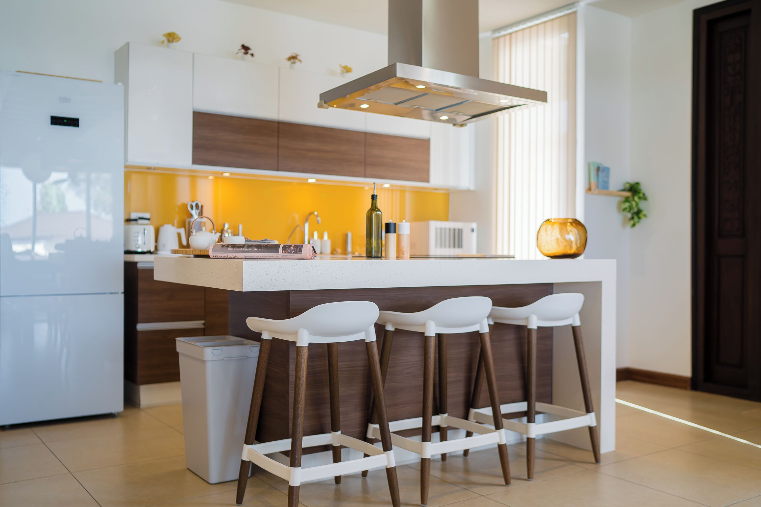 A modern kitchen with a central island, bar stools, a built-in oven, and a white refrigerator.